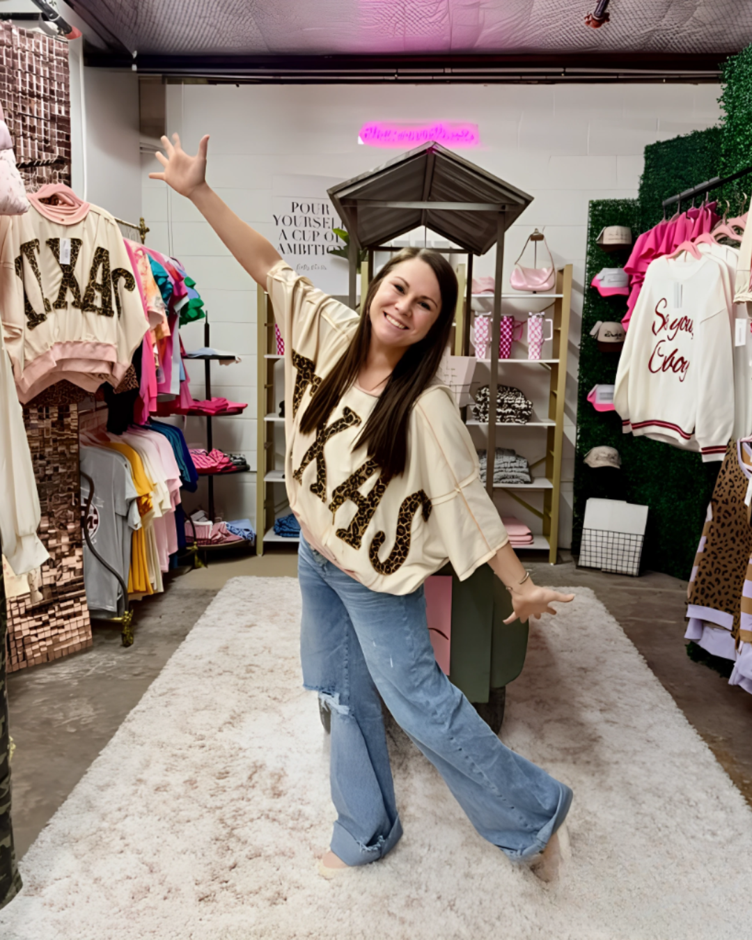 Woman in a store wearing a 'TEXAS' shirt, surrounded by clothing and decor.
